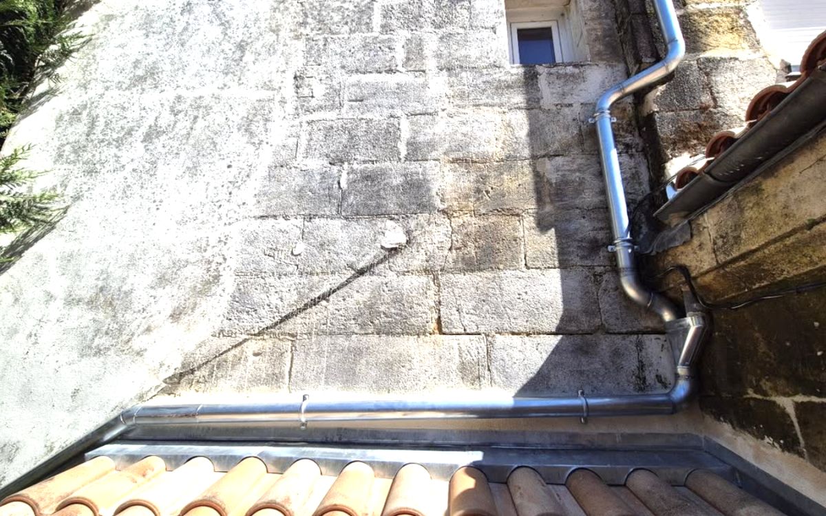 Gouttière et descente en zinc neuves le long d'un mur en pierre